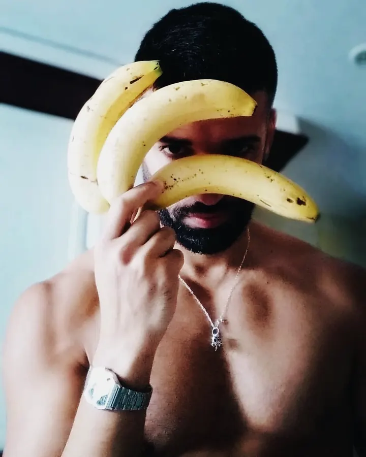 Homme torse nu, portant un collier, tenant trois bananes devant son visage