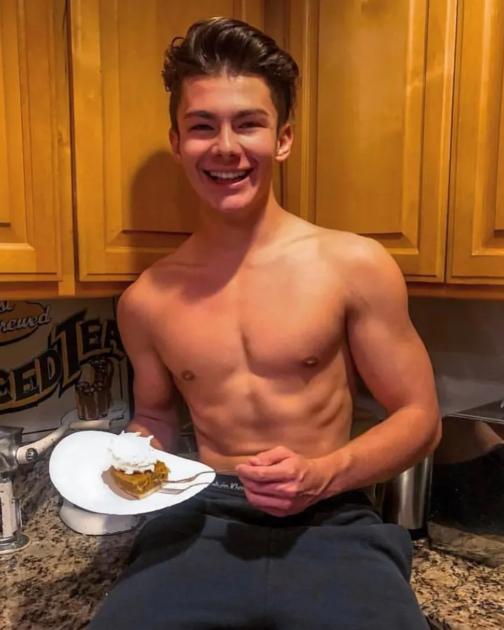 Homme torse nu, souriant, tenant une assiette avec un dessert, dans une cuisine