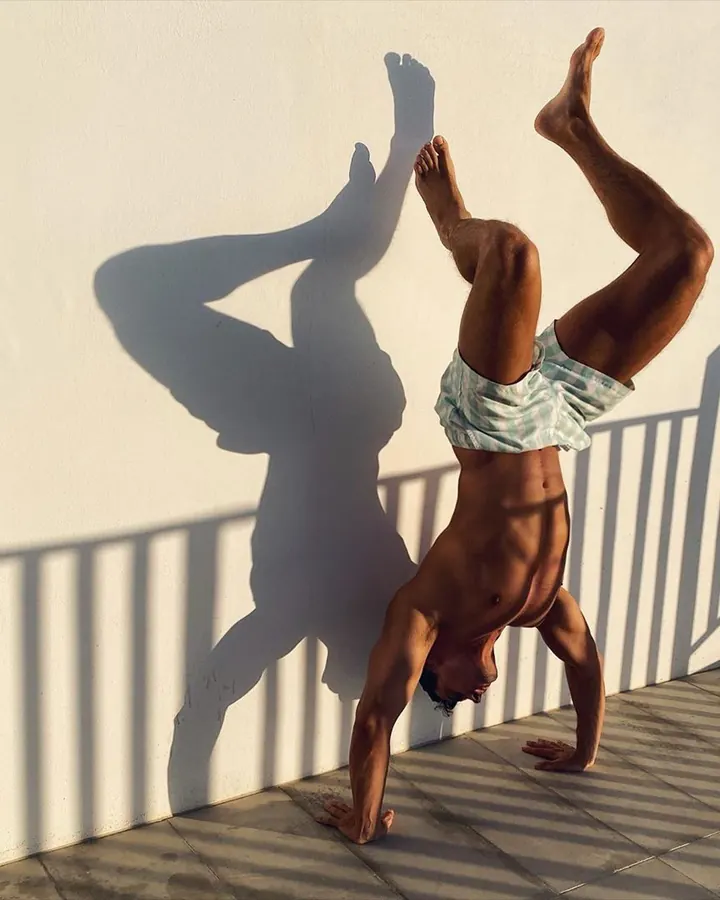 Homme torse nu, faisant un handstand contre un mur blanc, ombre projetée
