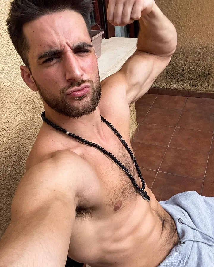 Homme torse nu, faisant un visage drôle, portant un collier noir avec une croix