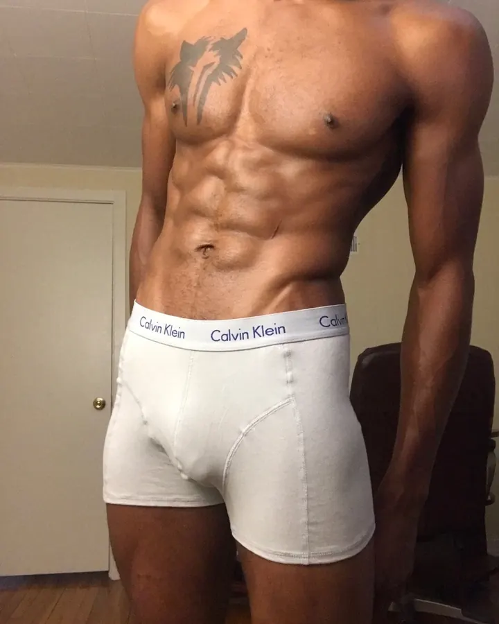 Homme barbu, torse nu, portant une bonnet russe noir et rouge, bras levés, muscles saillants, regard direct.