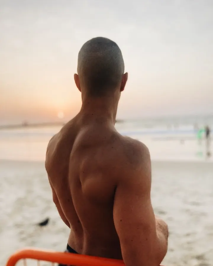 Homme de dos, torse nu, regardant le coucher de soleil sur une plage