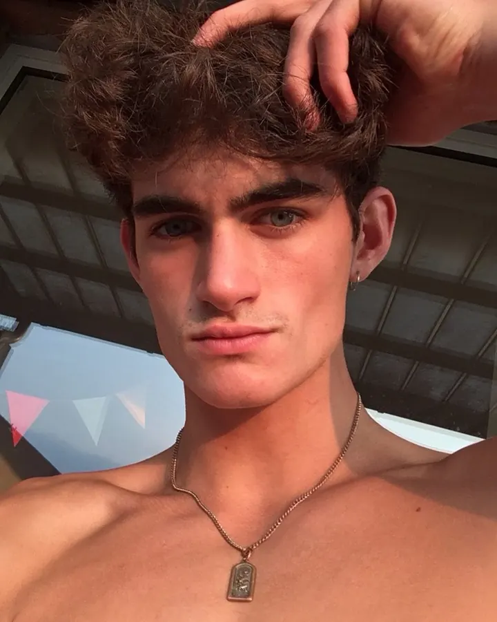 Jeune homme torse nu, portant un bonnet renversé, regardant vers le bas, devant une fenêtre