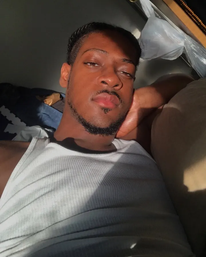 Homme torse nu, allongé sur un lit, regardant l'appareil photo avec un sourire doux.