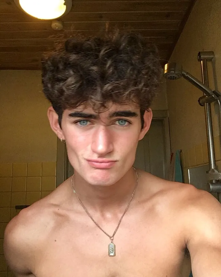 Jeune homme torse nu, cheveux bouclés, regardant l'appareil photo dans une salle de bain.