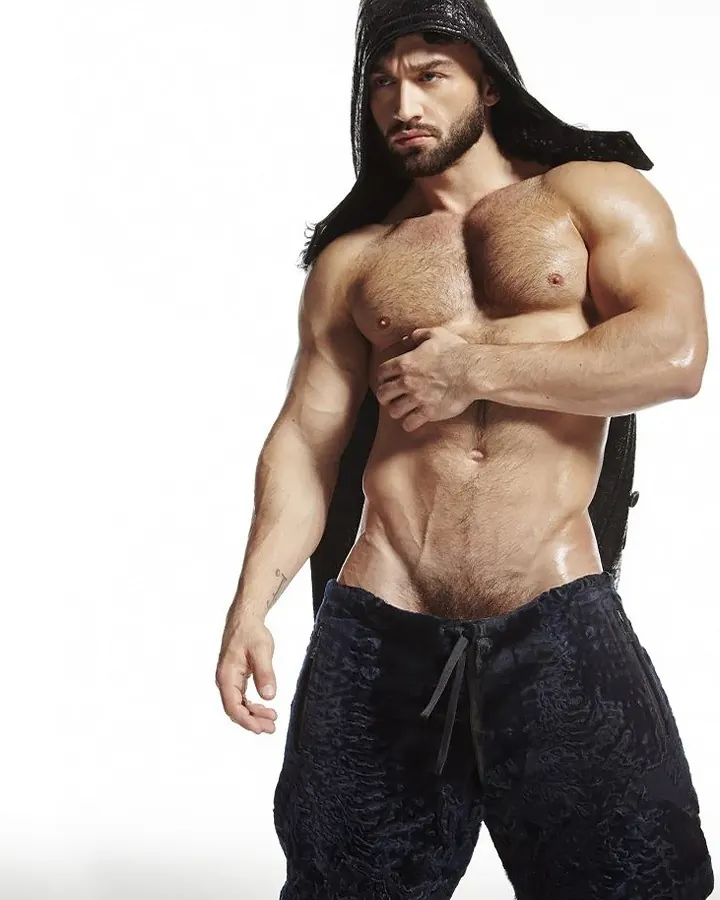 Homme musclé torse nu, portant un capuchon noir, posant sur fond blanc.