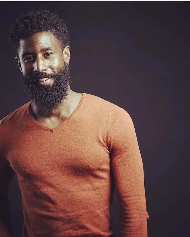 Homme africain barbu, torse nu, portant un slip noir, posant dans une piscine.