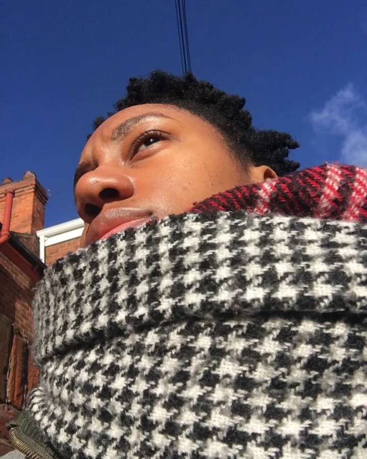 Homme africain aux cheveux courts, portant un foulard à motifs, regardant vers le haut sous un ciel bleu.
