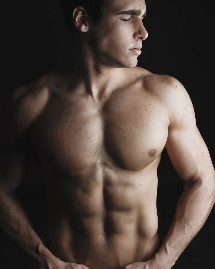 Homme blanc, torse nu, posant devant un arbre.