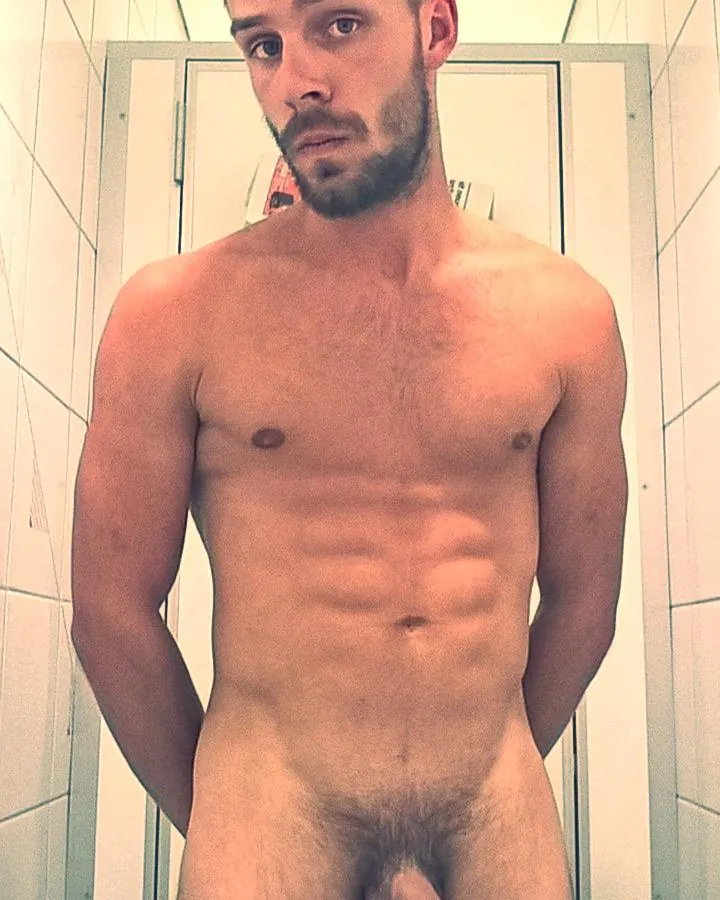 Homme blanc, torse nu, posant devant un arbre.