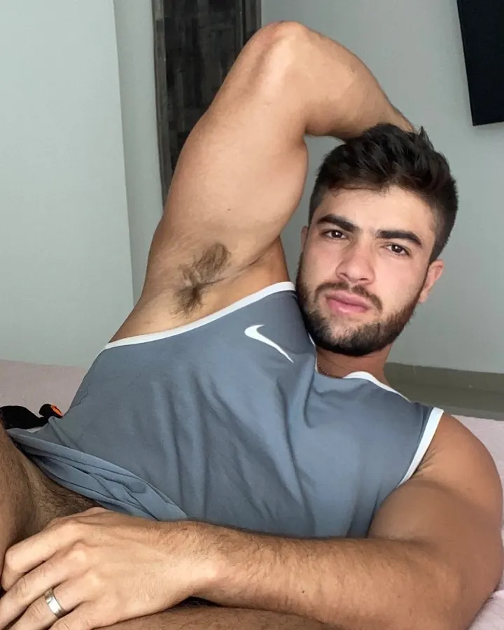 Homme blanc, torse nu, posant devant un arbre.