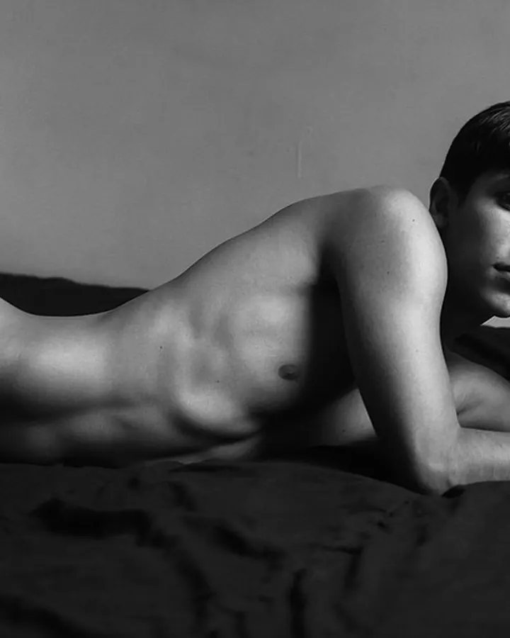 Homme torse nu, aux cheveux bruns, posant dans une lumière vive, regard intense.