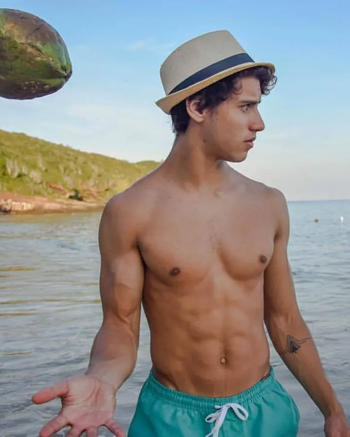 Homme torse nu, aux cheveux bruns, posant dans une lumière vive, regard intense.