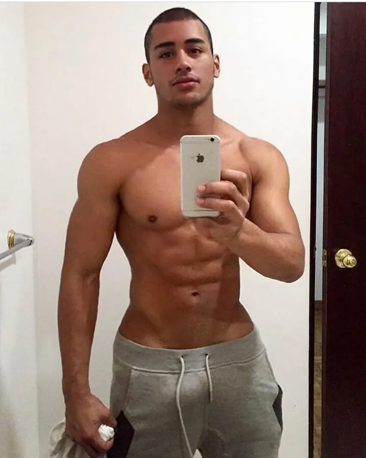 Homme torse nu en sweat gris, prenant un selfie dans un miroir, regardant directement l'appareil