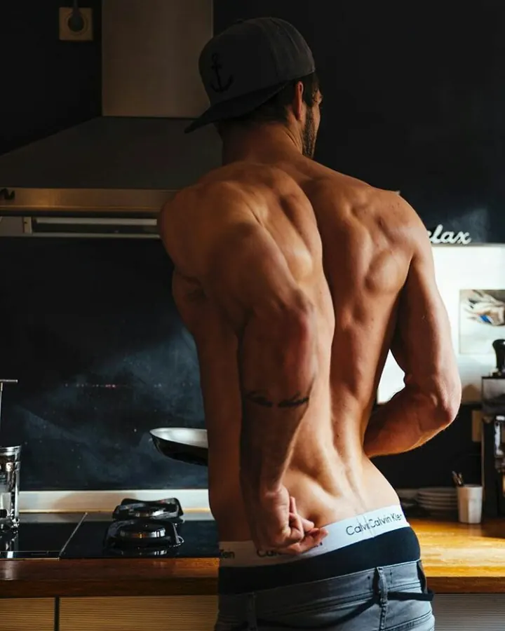 Homme torse nu, cheveux bruns, regardant directement l'objectif, dans un cadre sombre