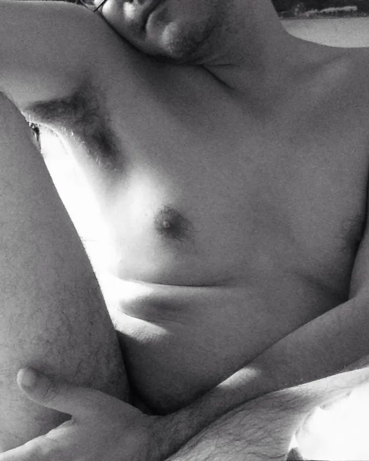Homme torse nu, cheveux bruns, regardant directement l'objectif, dans un cadre sombre