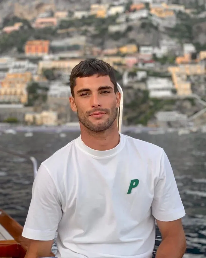 Homme latino en t-shirt blanc, souriant, devant une vue de ville sur la mer